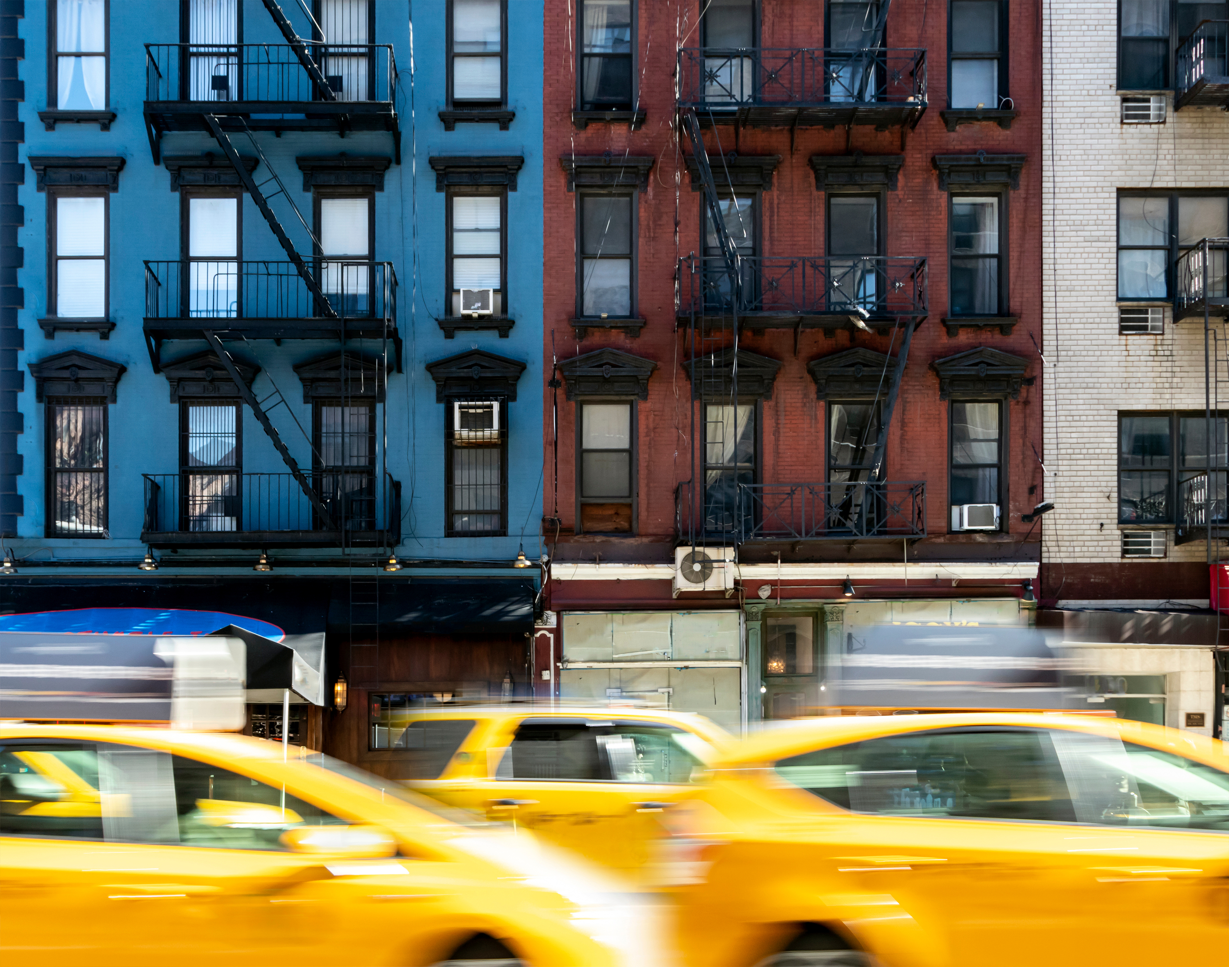 Blurry taxis in traffic in front of an apartment bulding.